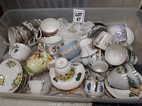Overhead view of a large plastic bin filled with mixed ceramic cups and saucers, various floral designs, pastel colors and gold trim visible.