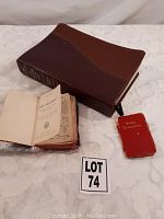 Brown hardcover Bible folded on side with two small well-worn Bible booklets beside it on cloth surface.