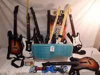 Photo showing five Band Hero guitar controllers in various colors, blue plastic storage container, and two music game packs.