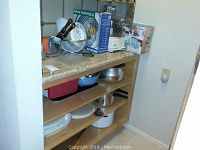 Overview of kitchen shelf with Duralex stackable glass bowls, salad tongs, cutting boards, pressure cooker, and storage containers on shelves