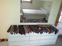 Full spread of assorted men's neckties laid out on two white dressers showing a variety of colors and patterns.