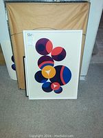 White-framed abstract geometric print featuring overlapping colored circles and triangular segments, front view