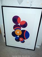 Framed Leon Polk Smith abstract print in black frame with white mat leaning against wall