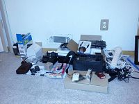 Wide shot of the lot showing various electronics including boxes, power strip, cables, and phones on a carpeted floor