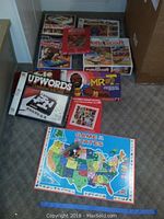 Wide shot of multiple boxed vintage family games including Game of the States board, Mr T board game, Upwords, Booby Trap, Potterycraft wheel, and stamp collecting kit.