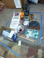 Wide view of lot arranged on floor showing the sundial, ceramic pots, watering cans, citronella candles, Gardening Made Easy note cards and other small items