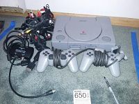 Sony PlayStation 1 console with two wired controllers and power adapter on carpet.