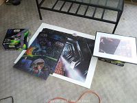 Overview of lot showing sealed Star Wars models, three mounted puzzles, and framed print on floor next to glass coffee table.