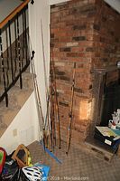 Fishing rods leaning against a brick wall near a staircase, showing overall quantity and variety.