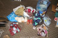 Various skeins of yarn in blue, red, and cream shades along with burlap fabric and macramé cord on carpeted floor.