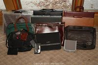 Full view of assorted men's briefcases, portfolios, laptop totes, passport covers, and wallets arranged on floor.
