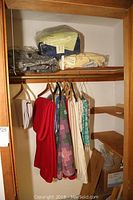 Linens folded and stacked on upper shelf with assorted linens hanging on wooden hangers in a closet space.