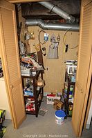 View inside a small closet showing multiple shelves loaded with various boxed and bagged hardware, as well as some tools and plastic storage units on floor and sides.