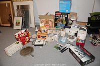 Overview photo showing a variety of small kitchen appliances including a coffee maker, yogurt maker, ice cream maker, cast iron pan, and multiple kitchen utensils and box packaging laid on floor.