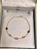 Photo of 14K gold chain bracelet with five colored stones laid flat in a display box.