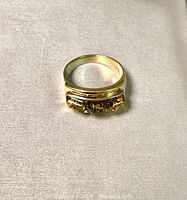 Front view of gold overlay sterling silver ring with three amber stones on light fabric background.