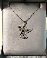Sterling silver angel pendant with open filigree wing design holding a 10K gold heart, displayed on fabric inside silver-toned jewelry box. Accompanied by a matching sterling silver chain.