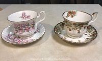 Two Royal Albert teacups and saucers displayed side by side on a table, showing floral patterns and gold trim.