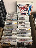 Photo showing a large collection of Nintendo Wii games stacked in rows with visible spines of cases and the boxed NHL Slapshot game on top.