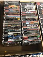 Over 60 PlayStation 2 games stacked in two columns inside a box showing a mixed variety of genres and titles in used condition.