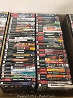 Photo showing over 60 PlayStation 2 game cases stacked in columns with visible titles covering racing, sports, action, and adventure genres.
