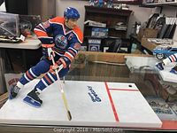 Angle showing mounted Wayne Gretzky figurine in Edmonton Oilers uniform posed on a hockey rink base with puck and stick.