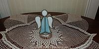 Front angle view of stained glass angel figurine placed on a crocheted doily covering a wood surface.