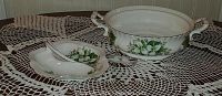 Both vegetable bowl and condiment dish shown on crochet cloth, highlighting the floral design and handles on the bowl.