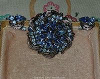 Close-up photo of vintage Jayflex sterling brooch and earrings set with sapphire blue rhinestones on a peach-colored fabric background inside a box.
