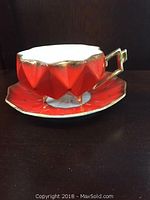 Side view of red geometric faceted vintage footed tea cup with gold trim and matching saucer