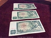 Three Czechoslovakia 100 Korun banknotes displayed on a dark fabric surface, showing front design with portraits and denomination.