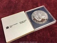 1988 Canadian silver dollar coin in protective plastic case with original Royal Canadian Mint box on red background.