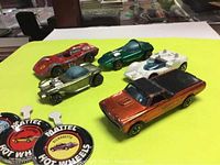 Top view of 5 Hot Wheels Redline die cast cars on yellow background with metal badges in front