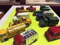 Overview of all 12 die cast toy trucks and vehicles arranged on a yellow surface showing various colors and vehicle types.