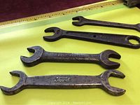 Four old open-ended wrenches on yellow background with ruler for size reference. All show wear and use.