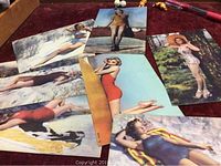 Photo showing all seven vintage pinup style postcards arranged on table.