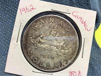 Close-up photo of the 1962 Canadian silver dollar coin showing the canoe design and handwritten notes on the holder.