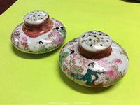 Pair of antique Asian hand-painted salt and pepper shakers on a yellow background.