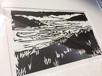 Framed black and white stone cut artwork depicting a riverside landscape with stylized natural elements.