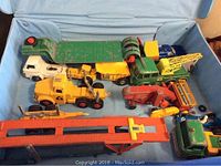Overview of various old die cast toy vehicles placed inside a case showing trucks, construction equipment and a car transporter in worn condition.
