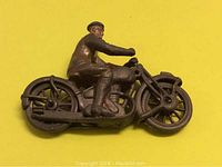 Left side view of antique cast iron toy motorcycle with rider on yellow background showing wheel detail and seated figure