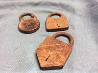 Three old rusted padlocks on blue fabric: round, rectangular, trapezoidal shapes all showing heavy rust and wear.