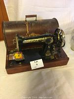 Front view of vintage black Singer sewing machine on wooden base with curved wooden case behind it.