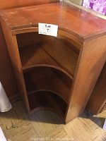 Front view of the wooden corner bookshelf showing three shelves and overall wear.