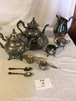 Full shot of the silver plate tea set including teapot, creamer, sugar bowl, metal strainers, spoons, and tray.
