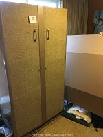 Front view of vintage metal wardrobe cabinet with two doors and two handles, showing textured light brown/gold finish and mirror on right door.