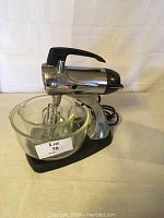 Full view of the vintage chrome and black Sunbeam Mixmaster stand mixer on black base with one large glass mixing bowl. Two metal beaters are installed in the mixer.
