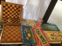 Lot of vintage board games on table, including Operation, Swamp Fox, Easy Money, Meet the Presidents, Huppe Mein Hutchen! and three wooden chess boards without pieces.