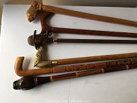 Photo showing all six decorative carved wooden canes laid flat, highlighting handle designs and shafts.
