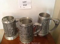 Photo showing all three pewter tankards side by side on a wooden surface with lot number tag visible.